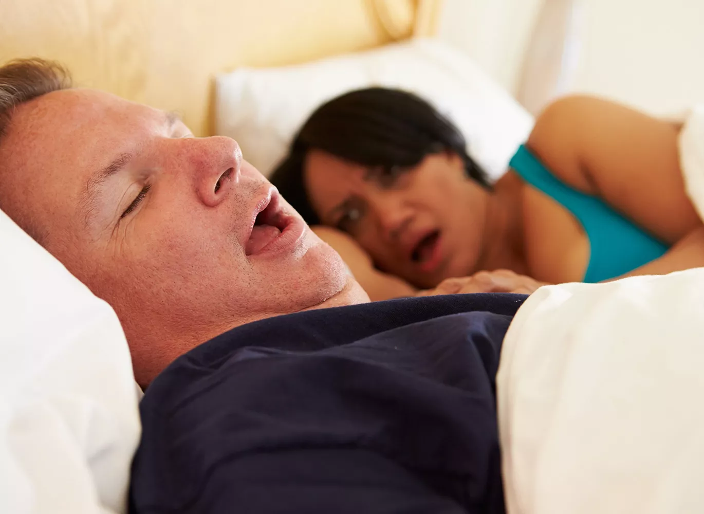 Man in bed snoring in his sleep while woman lays awake